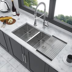 a stainless steel kitchen sink in front of a window with wine and bread on the counter