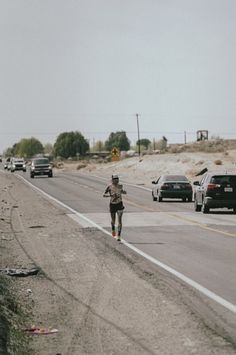 a man running down the road in front of cars on a highway with no traffic