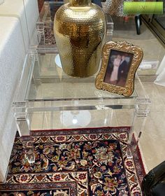 a glass table topped with a gold vase next to a rug and framed photo on it