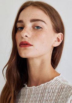 a woman with freckled hair and blue eyes looks off to the side while wearing a white sweater