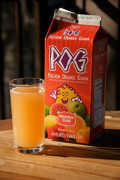 a glass of orange juice next to a carton of pxg on a table