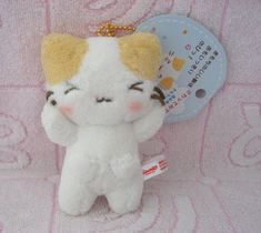 a small white and yellow stuffed animal on a pink blanket with a tag attached to it