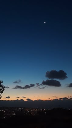 the moon is seen in the sky over a city at night with clouds and trees