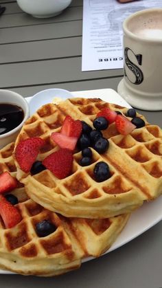 two waffles with strawberries and blueberries are on a plate next to a cup of coffee