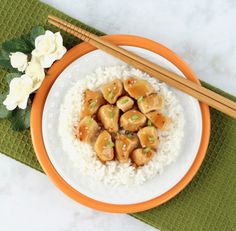 an orange and white plate topped with rice and meat next to chopsticks on a green place mat