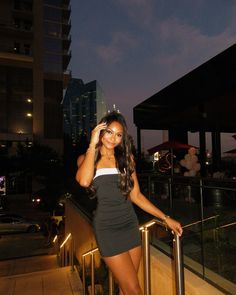 a beautiful young woman standing on top of a metal hand rail next to a tall building