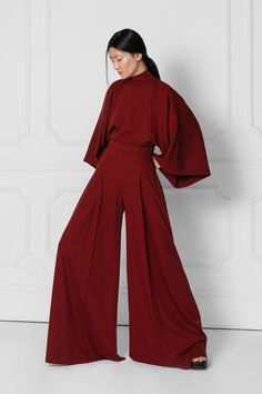 IO Jumpsuit features an exaggerated wide leg, pleat front detail and a high waist perfectly balanced out with traditionally tailored Kimono style sleeves and a high neck with 3 button closures at the back of the neck and an elegant open back.