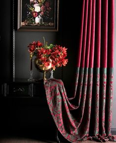 a vase filled with flowers sitting on top of a table next to a red curtain