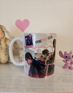 a coffee mug sitting on top of a table next to a small toy animal and a pink heart