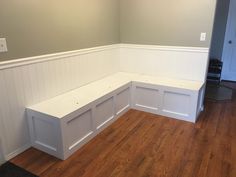 a corner bench in the middle of a room with wood floors and white paneling