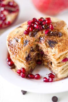 pancakes with pomegranates cut in half on a white plate next to an apple