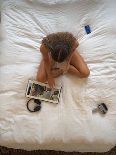 a woman laying on top of a white bed next to an open book and hair dryer