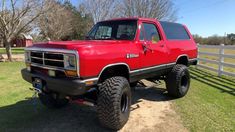 a red pick up truck parked on top of a dirt road next to a fence