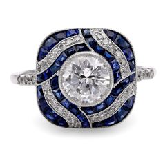 Center Stone: Diamond Cut: Round Brilliant Cut Weight: 0.97 Carat Color: J Clarity: SI Accent Stone: 40 Sapphires Cut: Calibre Cut Weight: Approximately 0.5 Carats Color: Blue Accent Stone: 34 Diamonds Cut: Old European and Round Brilliant Cuts Weight: Approximately 0.3 Carats Color: H Clarity: VS Metal: Platinum Era: Modern Circa: 2020's in the Style of Art Deco Hallmarks: Stone Weight Engraved Size: 6 3/4 and can be resized Gram weight: 6.12 This modern ring, inspired by the timeless elegance Dazzling Multi-stone Platinum Diamond Ring, Art Deco Multi-stone Platinum Diamond Ring, Round Multi-stone Platinum Diamond Ring, Platinum Multi-stone Diamond Ring With Round Shape, Multi-stone Platinum Diamond Ring, Multi-stone Round Sapphire Ring In Platinum, Classic Multi-stone Platinum Diamond Ring, Formal Multi-stone Halo Ring, Dazzling Platinum Sapphire Ring