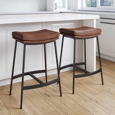 two brown stools sitting on top of a wooden floor next to a white counter