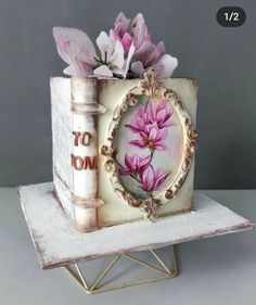 there is a small box with flowers in it on top of a stand that has a book