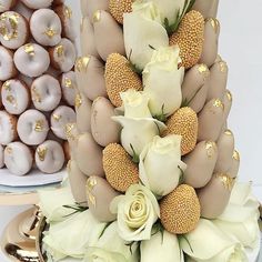 a three tiered cake decorated with white flowers and gold decorations on plates next to doughnuts