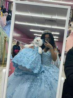 a woman taking a selfie in front of a mirror with a teddy bear wearing a blue dress