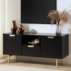 a black and gold sideboard with two vases on it in front of a flat screen tv