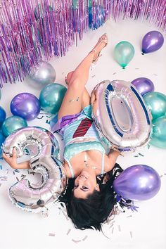 a woman laying on the ground surrounded by balloons and streamers with her legs spread out