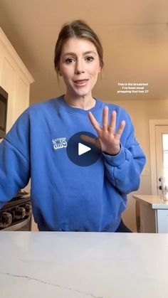 a woman standing in front of a kitchen counter with her hand up to the camera