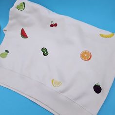 a white t - shirt with fruit on it sitting on top of a blue surface