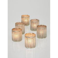 three glass candle holders sitting next to each other on a white surface with light coming from them