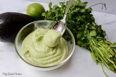 an avocado dip in a bowl next to some cilantro and limes