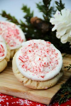 three cookies with white frosting and red sprinkles on a cutting board