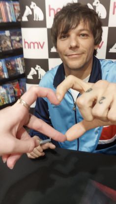 a man sitting at a table with two fingers in the shape of a heart and an arrow