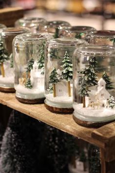 several glass jars with snow and trees in them