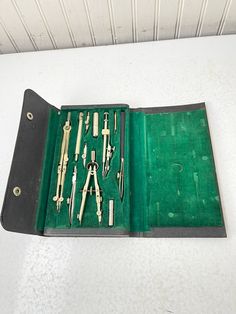 an open green leather case with tools in it on a white table top next to a wall