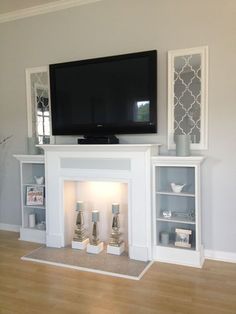 a flat screen tv mounted on the wall above a fireplace with candles and vases