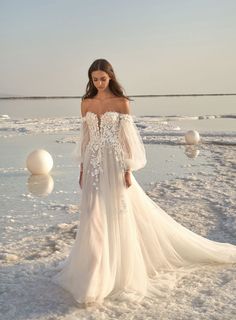 a woman standing in the snow wearing an off shoulder wedding dress with long sleeves and flowers on it