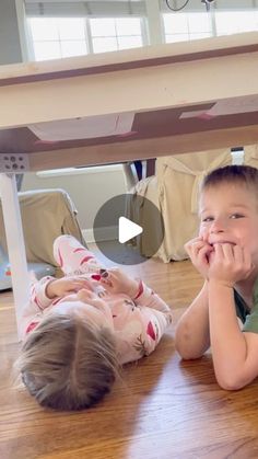 two young children laying on the floor under a table with their hands in their mouths