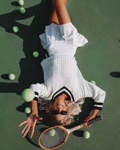 a woman laying on top of a tennis court holding a racquet and ball