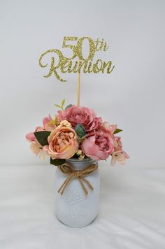 a bouquet of flowers in a mason jar with a cake topper that reads 50 th reunion