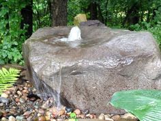 a large rock with water coming out of it in the middle of some rocks and plants