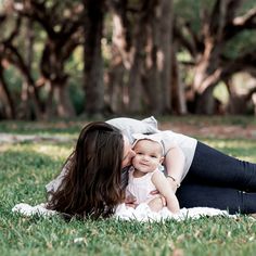 a woman laying on top of a grass covered field holding a baby