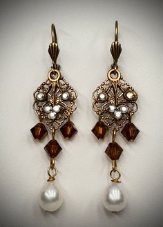 Fresh water pearls, Smokey topaz Swarovski crystal beads and a lovely crystal leaf design make up the design of these lovely handcrafted brass with brass plated earrings. These filigree chandelier earrings have three crystal brown beads, multi color clear crystal stones on a leaf that moves with a freshwater pearl drop. They are about 2 1/2" long-see the photo (the filler photo is the same style but a different color than this listing). Sporting a lever back earring wire  with a decorative front Elegant Copper Earrings With Dangling Beads, Elegant Beaded Copper Jewelry, Elegant Antique Gold Brass Chandelier Earrings, Elegant Beaded Brass Chandelier Earrings, Elegant Bronze Earrings With Dangling Beads, Elegant Handmade Copper Chandelier Earrings, Elegant Brown Brass Earrings, Victorian Gold Metal Chandelier Earrings, Elegant Metal Crystal Earrings With Dangling Beads