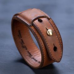 a brown leather bracelet with two brass buttons