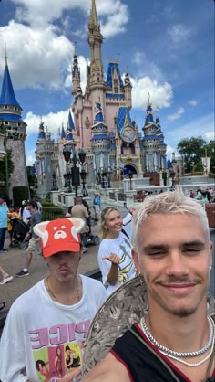 a man with white hair wearing a mickey mouse hat in front of a castle at disneyland