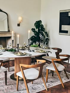 a dining room table is set with plates, glasses and candles in front of a fireplace