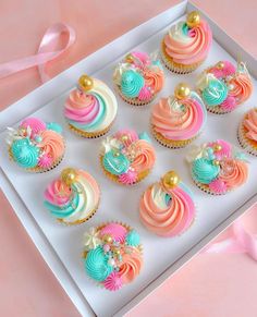 cupcakes decorated with pastel colors and gold decorations in a white box on a pink background