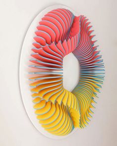 an art piece made out of colored paper on a white wall with a circular hole in the center