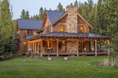 a log home with lights on the front porch and covered in grass, surrounded by trees