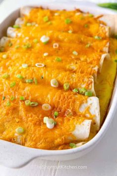 an enchilada dish in a white casserole dish with green onions and cheese