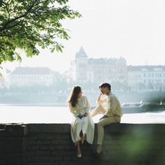 a man and woman sitting on a wall next to each other looking at each other