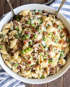 a bowl filled with pasta and peas on top of a striped table cloth next to a fork