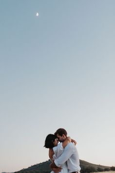 a man and woman embracing each other in front of the ocean under a clear blue sky